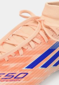 Botín de fútbol naranja con una parte superior texturizada, que presenta acentos azules y un ajuste ceñido. Cierre de cordones con un cuello tipo calcetín para mayor soporte.