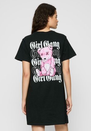 Svart t-skjorte med kort erm, med et stort rosa bjørn-grafikk og "Girl Gang" tekst på baksiden. Kvalitet i bomull, avslappet passform.