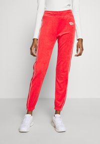 Röda velour joggers med vita sidostrick, elastisk midja och muddar vid anklarna. Litet Nike-logotyp på vänster lår.