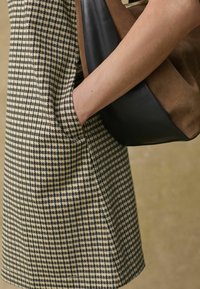 Odzież w wzór houndstooth w kolorze beżowym i czarnym, z kieszonką. Widoczna jest również torebka z brązowej i czarnej skóry.