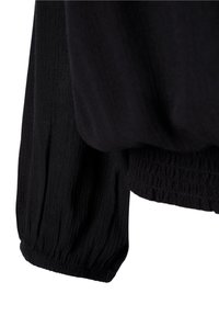 Haut noir à manches longues avec un tissu texturé ; doté d'un poignet froncé et élastiqué pour une coupe légèrement ajustée au niveau du poignet.