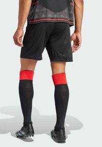 Bermudas deportivas negras combinadas con calcetas negras que tienen acentos rojos. Diseño estructurado con patrones texturizados en las bermudas. Zapatillas negras.