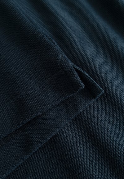 Tessuto blu navy scuro con un pattern struttura a coste. Due sezioni piegate si sovrappongono, mettendo in mostra i dettagli delle cuciture lungo i bordi.
