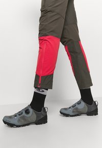 Szare i czarne buty turystyczne z siateczkową fakturą, okrągłym noskiem i systemem zapinania na pokrętło. Połączone z ciemnymi spodniami i czarnymi skarpetami.