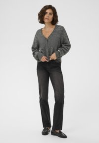 Harmaa neulecardigan, jossa on v-pääntie, nappikiinnitys ja puffihihat, yhdistettynä tummiin suoriin farkkuihin ja mustiin loafereihin.