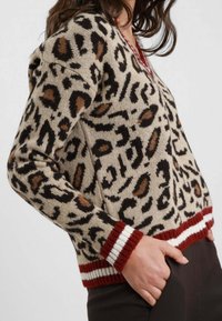 Maglione a stampa leopardata beige, con macchie marrone scuro e arancioni. Accenti a coste rossi e bianchi sui polsini e sull'orlo. Materiale in maglia morbida.