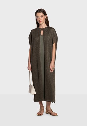 Ruskea kudottu kaftaani, jossa on avainreikäkaula-aukko, yhdistetty vihreään mekkoon. Malli pitää valkoista laukkua ja käyttää kullanvärisiä sandaaleja.