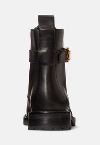 Bota de tornozelo em couro preto com detalhe de fivela, bico arredondado e sola robusta. Textura suave com acabamento fosco.