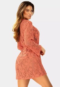 Koronkowa sukienka w kolorze koralowym z długimi dzwonowymi rękawami, z kwiatowymi wzorami i luźnym krojem, długość powyżej kolana, z otwartą strukturą tkaniny.