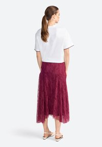 Haut blanc à manches courtes avec un bord festonné, associé à une jupe en dentelle bordeaux ornée de motifs floraux complexes. Des chaussures légères complètent le look.