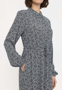 Blumenmuster langärmeliges Kleid in Schwarz und Weiß, mit Kragen, elastischer Taille und seitlichen Taschen, das ein kleines Blumenmuster aufweist.