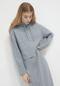 Hoodie grigio, corto, realizzato in morbido tessuto testurizzato. Presenta un cappuccio con coulisse e polsini a costine. Abbinato a un vestito grigio coordinato.