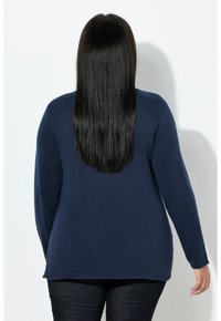 Maglione a maglia blu navy con maniche lunghe, consistenza a coste, orlo arrotondato, indossato con jeans scuri. Il design è casual e aderente sulle spalle.