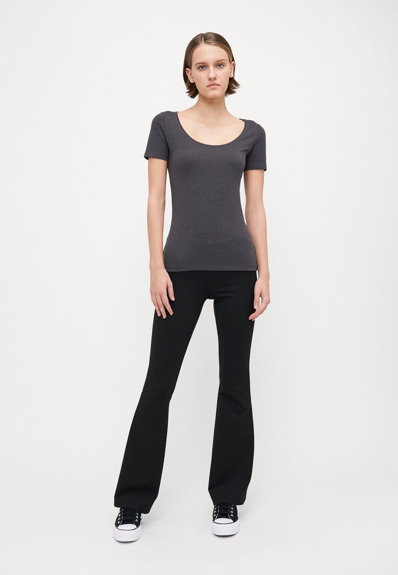 Camiseta ajustada de manga corta gris con escote redondo, combinada con pantalones de campana negros y zapatillas blancas. Textura simple y suave.