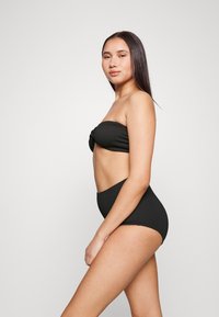 Conjunto de bikini preto com um top sem alças e uma frente torcida, acompanhado de calças de cintura alta, feito de um tecido texturizado.