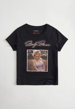 Schwarzes T-Shirt mit kurzen Ärmeln, das eine lächelnde Frau in einem Vintage-Kleid mit Blume im Haar zeigt, und stilisierter Schrift über dem Bild.