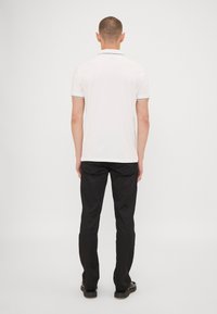 Hvit polo skjorte med korte ermer, svart kanting på krage og ermer, kombinert med svarte bukser. Enkle, rene linjer og en tettsittende design.