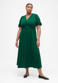 Roheline põlveni ulatuv kleit V-kaelusega, puffvarrukatega ja nööpdetailiga rinnal. Pehme tekstuur ja voolav siluett.