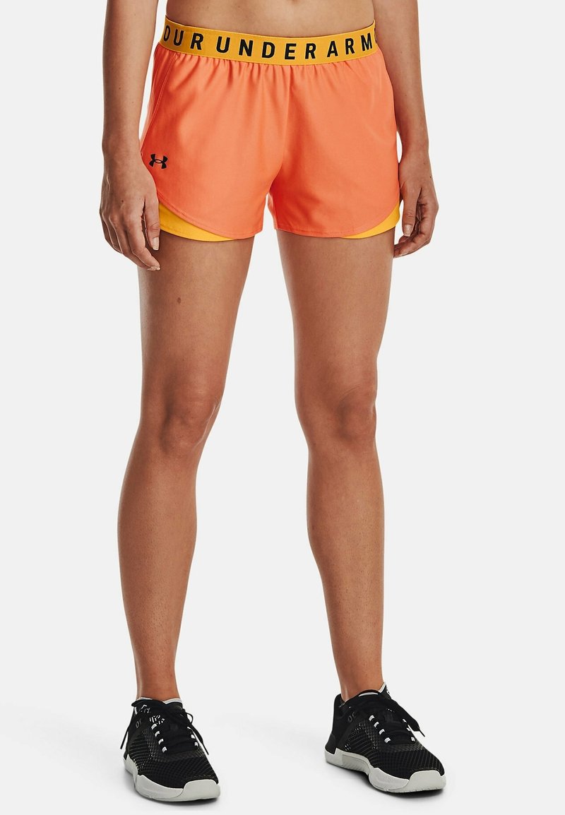 Orange atletshorts med gul innerfoder, utrustade med ett svart elastiskt midjeband med texten "UNDER ARMOUR". Lättviktigt tyg och lös passform.