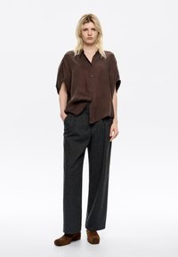 Brown short-sleeve button-up shirt paired with gray high-waisted trousers and brown suede shoes. Soft fabric texture and relaxed fit.