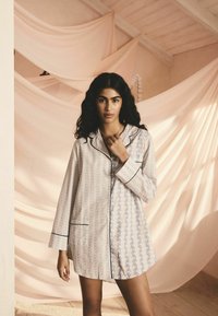 Keve pajama berlainan polka yang menampilkan campuran garis tegak dan corak bunga, dengan pinggiran hitam dan potongan yang santai.