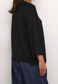 Schwarzes, locker sitzendes Oberteil mit 3/4-Ärmeln, weicher Textur, rundem Halsausschnitt und fließender Silhouette, kombiniert mit Jeanshose.