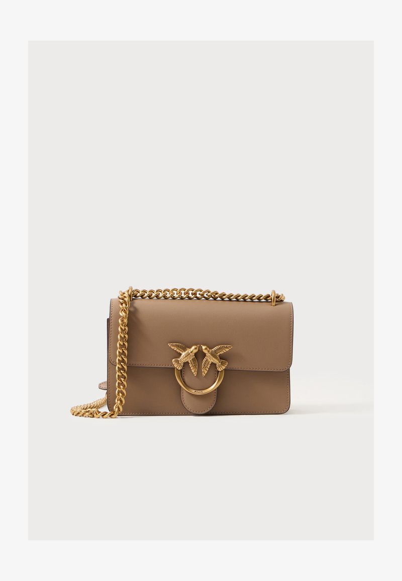 Bolsa de mão em pele castanha com fecho de aba, apresentando um contraste em metal dourado com dois pássaros e uma alça em corrente. Textura suave, forma compacta.