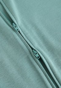 Deux fermetures éclair adjacentes de couleur sarcelle sur un tissu doux, partiellement fermées, mettant en valeur le design de la fermeture éclair et la texture du matériau.