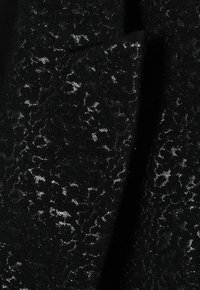 Schwarzer Stoff mit einem strukturierten Spitzenmuster in einem dezenten silbernen Faden, mit einer weichen, samtigen Oberfläche und filigranen Details.