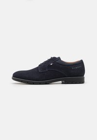 Zapatos de ante azul marino con cordones y una superficie texturizada, que cuentan con una suela de goma y un sutil logo de la marca en el tacón.