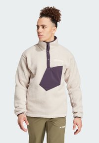 Pullover in pile color crema con tasca frontale e dettagli sul colletto in viola. Presenta bottoni a pressione e una superficie testurizzata.