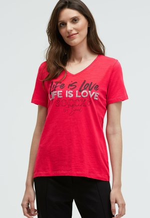 Red V-neck t-shirt in soft fabric features a printed design with the text “Life is Love” in black and silver accents. Short sleeves.
