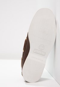 Semelle d'une chaussure Timberland marron avec une semelle extérieure blanche non marquante montrant le logo et un motif de grip texturé.