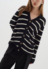 Marinblå och crème randig cardigan med V-ringning, knäppning och avslappnad passform. Tillverkad av mjukt material med en texturerad yta.