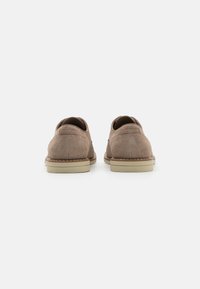 Zapatos de ante marrón con punta redondeada. Suela de goma ligera, costuras en contraste y un diseño típico de perfil bajo.