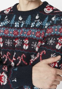 Mörkblå stickad tröja med festliga mönster i rött, vitt och blått, inklusive snögubbar, träd och godiskäppar. Ribbad halsringning och ärmslut.