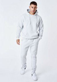 Lichtgrijze hoodie met een voorzak en koordjes, gecombineerd met bijpassende sweatpants met elastische boorden en witte sneakers.