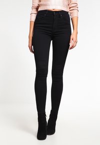 Jeans skinny de tiro alto negros con una tela suave y elástica y un ajuste elegante. Presentan un clásico diseño de cinco bolsillos y costuras sutiles.