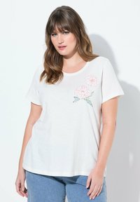 Camiseta blanca de manga corta, cuello redondo, con bordado floral rosa en la parte superior izquierda; tela suave, ajuste relajado.