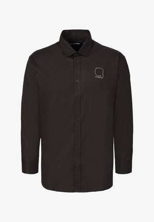 Chemise noire à manches longues avec boutons, col pointu et petit logo doré en contour représentant une silhouette de tête sur la poitrine gauche.