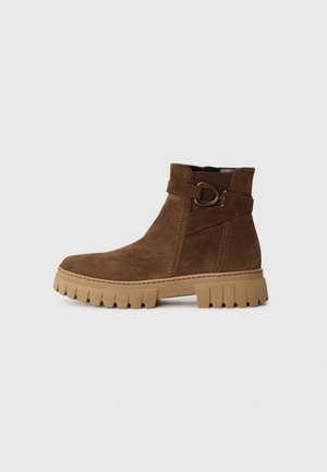 Brown suede ankle boot with a soft texture, rubber lug sole, and decorative strap featuring a metal buckle accent.
