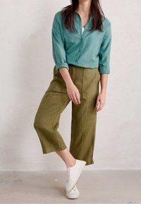 Turquoise gestreepte overhem met opgerolde mouwen, gecombineerd met olijfgroene wijde, cropped broek en witte veterschoenen.