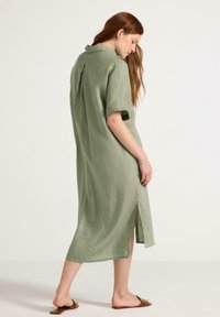 Grön linnéklänning med korta ärmar, slits bak, krage med knappar och raka linjer. Bärs med enkla bruna sandaler.
