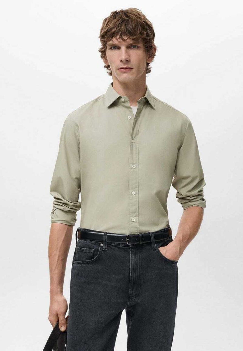 Camisa verde claro de botones con mangas remangadas y textura suave, combinada con vaqueros oscuros y cinturón negro, mostrada en un modelo masculino.