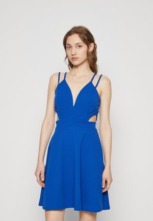 Blue dress featuring a deep V-neckline, thin straps, cut-out sides, and a flared skirt. Made of smooth, lightweight fabric.