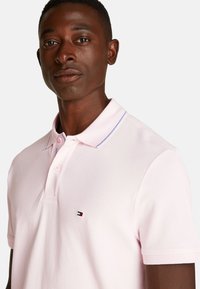 Polo de color rosa claro con tejido texturizado, tapeta de dos botones y un cuello con un acento azul. Logo bordado en el pecho.