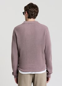 Maglione a maniche lunghe in maglia color malva chiaro, con trama a coste e colletto. Indossato sopra una camicia bianca, abbinato a pantaloni in tonalità neutre.