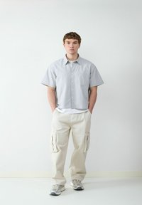 Grijze geruite overhemd met korte mouwen en een zak, gecombineerd met crème kleurige, losse cargobroek met zijzakken en grijze sneakers.