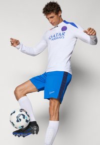 White long-sleeve football shirt with blue accents and "Qatar Airways" logo, paired with blue shorts, black and blue cleats, and white socks.