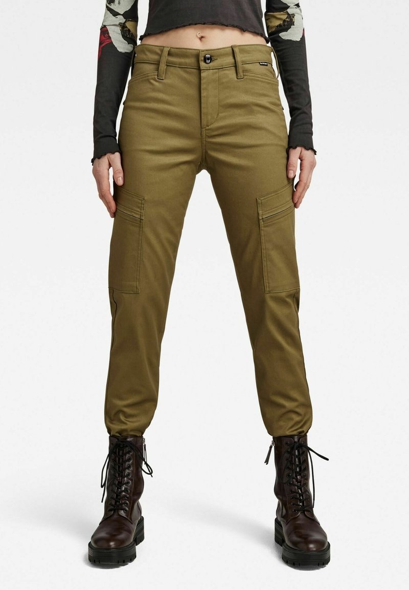 Pantalons cargo verts olive avec une coupe ajustée, dotés de poches latérales et d'une fermeture à bouton. Fabriqués en tissu résistant, associés à des bottes à lacets noires.
